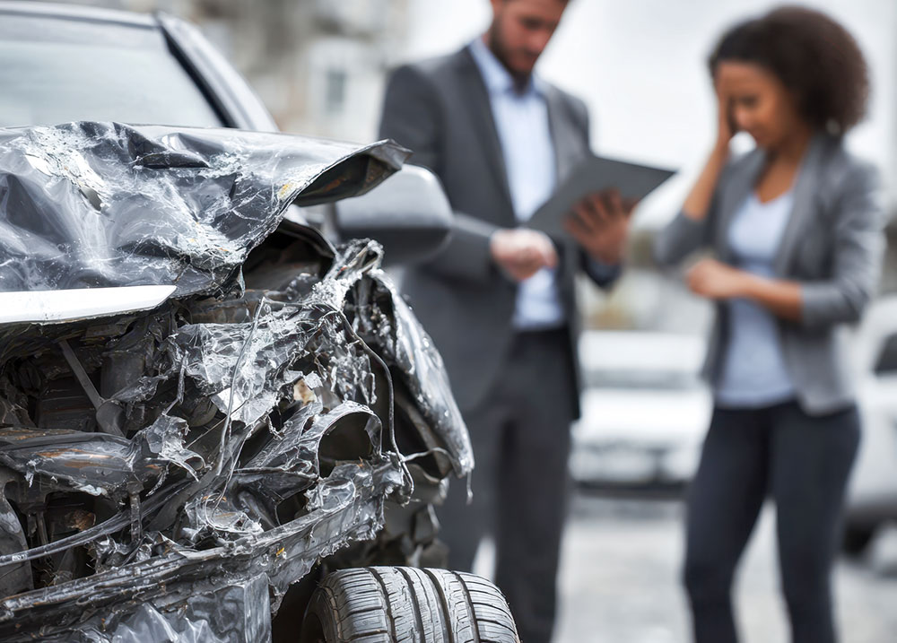 Damaged front end of a car with people discussing the crash on a city street, showing why you should contact a Nevada car accident lawyer quickly.